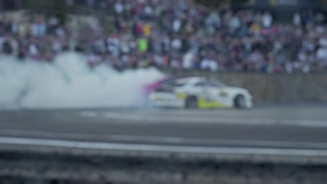 2 cars drift on sharp tight turn on asphalt road during show. Smoke from under wheels. Tire burnout. Racing competitions in slow motion. Crowd of spectators watches performance. Blurred. Extreme drive