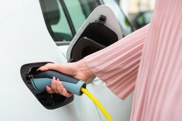 Female hand, opening a socket cover and plugging in the charger in an electric car at a charging...