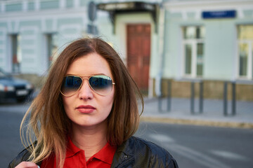 Woman in red polo and black jacket and sunglasses standing on the street