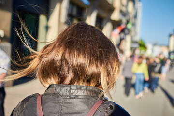 Rear view of the woman with brown hair and walking on the city street