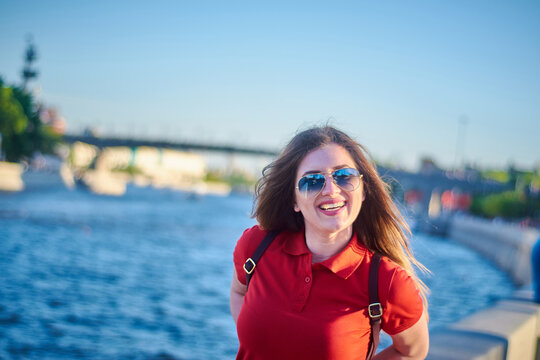 A laughing woman on the embankment in a red polo and sunglasses