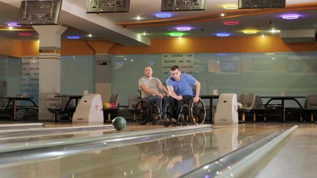 Two young disabled men in wheelchairs playing bowling in the club