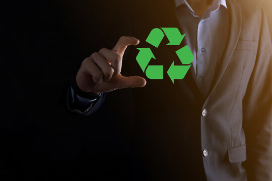Businessman in suit over dark background holds an recycling icon, sign in his hands. Ecology, environment and conservation concept. Neon red blue light