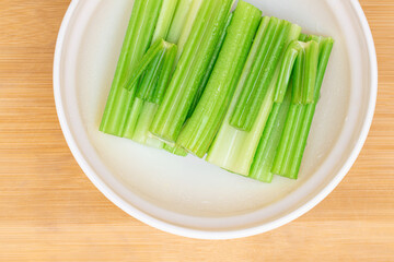 Fresh Chopped Celery Sticks with Water Drops in White Bowl on Bamboo Cutting Board - Top View....