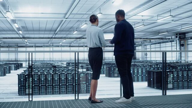 Data Center Female System Administrator and Male IT Specialist Talk, Use Laptop. Information Technology Engineers work on Cyber Security Network Protection in Cloud Computing Server Farm.