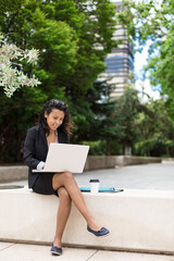 Young latin american woman using a laptop computer outdoors. Space for text.
