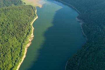 Top down aerial view of big lake with clear blue water between high mountain hills covered with...