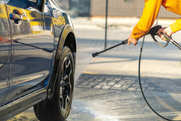 Closeup of male driver washing his car with contactless high pressure water jet in self service car wash.