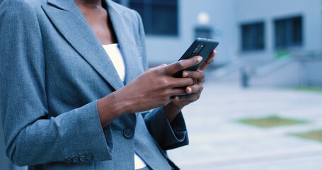 Being always in touch. Qualified young optimistic multiracial woman with short haircut is reading emails using smartphone. She is expressing gladness while standing with gadget in the street