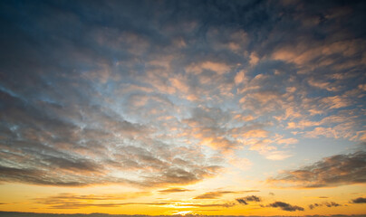 Dramatic sunset landscape with puffy clouds lit by orange setting sun and blue sky.