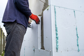 Construction worker installing styrofoam insulation sheets on house facade wall for thermal protection. - obrazy, fototapety, plakaty