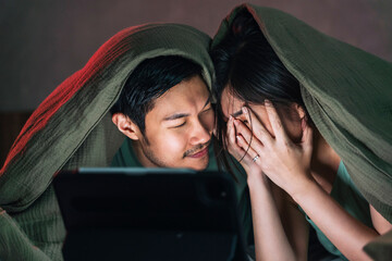 asian adult lover marry couple enjoy watching horror online movie from laptop or tablet in blanket...