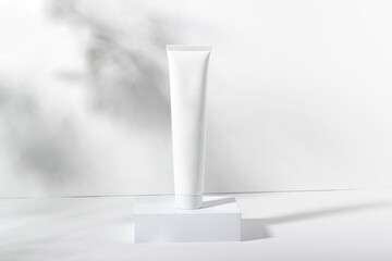 White cosmetic tube on a stand with leaves and shadows. Toothpaste, face and body cream. Female cosmetic tube with skin care product. Organic cosmetics. Copy space.