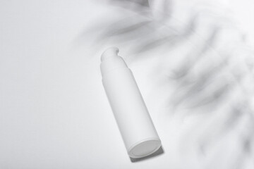 Cosmetic cream or mask in a white tube with hard shadows from the leaves on a white background. Natural organic care for face and body skin. View from above.