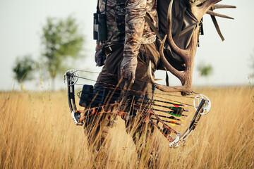 Close up shot of a hunter dressed in camouflage clothing holding a modern bow. - obrazy, fototapety, plakaty