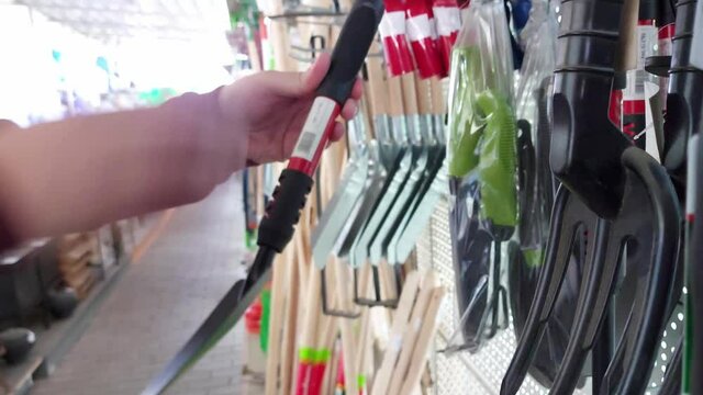 A man chooses garden products in the department of a hypermarket. Garden shovels for planting plants, close-up
