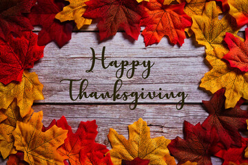 Happy Thanksgiving sign on wooden background surrounded by colorful maple leaves. Autumn & fall...
