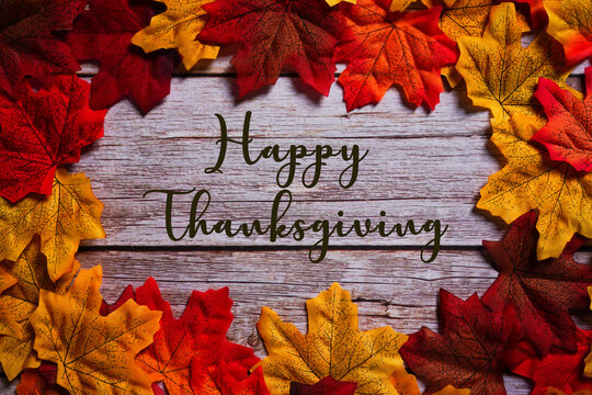 Happy Thanksgiving sign on wooden background surrounded by colorful maple leaves. Autumn & fall holiday composition.