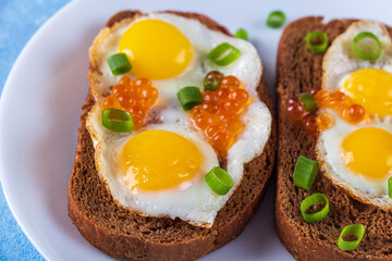 Home cooking. Whole grains Bruschettas with Fried Quail Eggs with green onions and with red caviar on plate. Balanced breakfast.