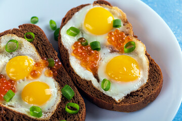 Home cooking. Whole grains Bruschettas with Fried Quail Eggs with green onions and with red caviar on plate. Balanced breakfast.