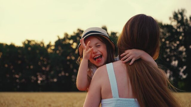 Slow Motion Mom Holding Daughter In Arms And Running In Wheat Field At Sunset. Following Shot Happy Child Making Faces And Laughing At Camera. Concept Of Fun