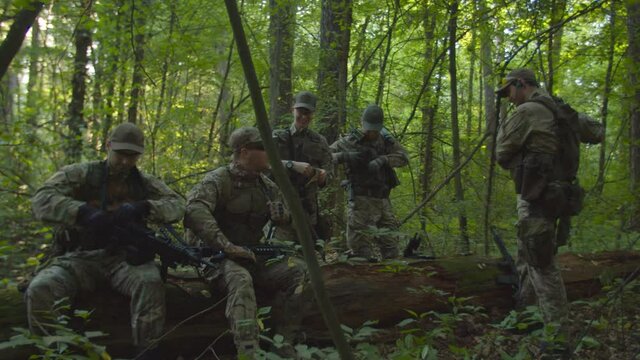 Fully armed anti-terrorism unit getting ready to military operation in forest at daybreak. Professional soldiers checking ammunition, charging weapon, preparing to fight