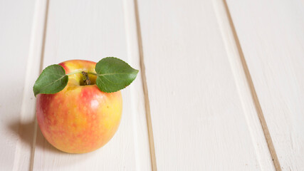 One bright ripe apple with leaves on a white table