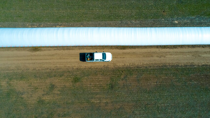 Aerial view of 4x4 pickup truck driving through wheat crops field with silos bags on the road. Argentina © claudio