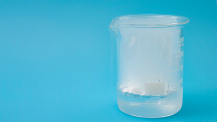 Science laboratory, scientific experiment and lab test concept with dry ice in a glass chemistry beaker isolated on blue background with copy space