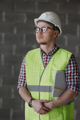 portrait of a male engineer at work, a European male designer or architect at the site, the work of a qualified and confident engineer in glasses and white helmet, engineering on large construction