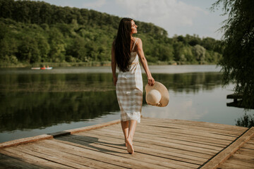 Relaxing young woman standing on wooden pier at the lake