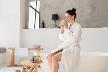 Young beautiful woman having breakfast at home in bathrobe, preparing for taking shower bath. Body...