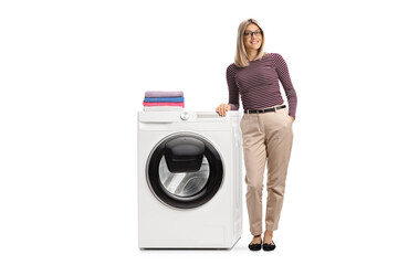 Full length portrait of a young woman leaning on a washing machine with folded clothes on top