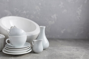 Empty crockery set or ceramic dishes. White kitchen dishware and tableware on table near grey wall