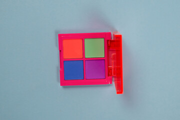 Obraz premium Purple, green, orange and blue eye shadow palette isolated on a blue background. Make up. Neon colours.