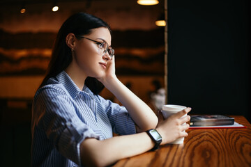 Side view portrait business woman sitting cafe drink hot beverage coffee break have lunch smart watch hand wear stylish glasses looking away book wooden table copyspace. Student documents papers