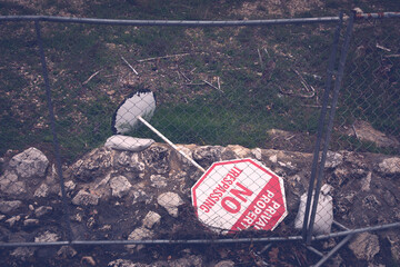 No trespassing sign turned over behind a fence