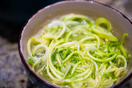 Closeup of shredded spiralized zucchini or cucumber raw noodles pasta for raw vegan cooking preparation or low-carb substitution of soup with water broth