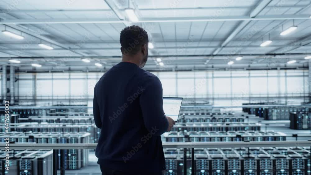 Fototapete Data Center Engineer Using Laptop Computer. Server Farm Cloud Computing Specialist Facility with Black Male System Administrator Working with Data Protection Network for Cyber Security.