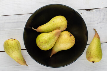 Several organic ripe pears on a ceramic platter on a wooden table, close-up, top view.