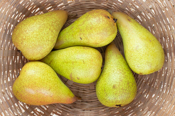 Several organic ripe pears on straw dishes, close-up, top view.