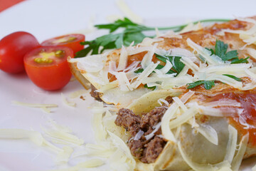 Pancakes with meat, in tomato sauce and cheese, with cilantro and grated cheese on top, and some cherry tomatoes on the plate.