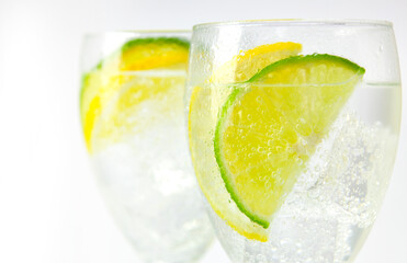 Two stemmed glasses with sparkling ice water and lemon and lime slices on white