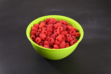 Ripe raspberry in a green plate on dark background.