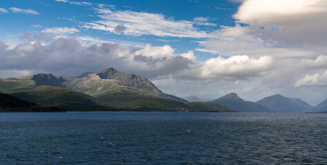 panorama view of a rugged and wild coastline with mountains and stormy seas with whitecaps under and expressive cloudy sky