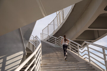 Obraz na płótnie Canvas An athlete girl runs up the stairs of the bridge. Evening strength running workout in the city. Preparing for the competition.