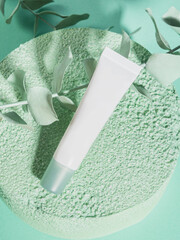 White generic cream tube on green textured podium on monochrome background