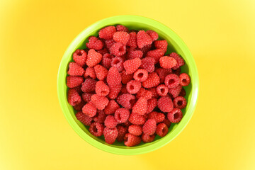 Ripe raspberry in a green plate on yellow background.