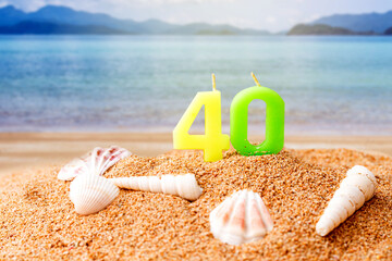 candle number 40 and sea shell over blurred blue sea and sand beach with clear blue sky on day noon...