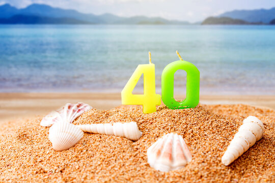 candle number 40 and sea shell over blurred blue sea and sand beach with clear blue sky on day noon light.